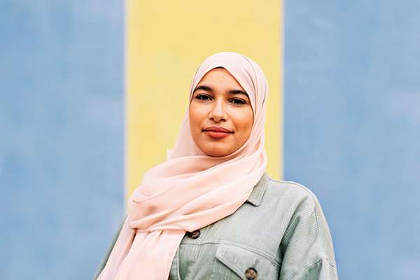 A happy woman wearing a light peach-colored hijab and a light sage-green jacket