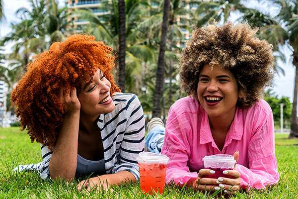 Young Latinx women talking lying on grass in Miami, Usa