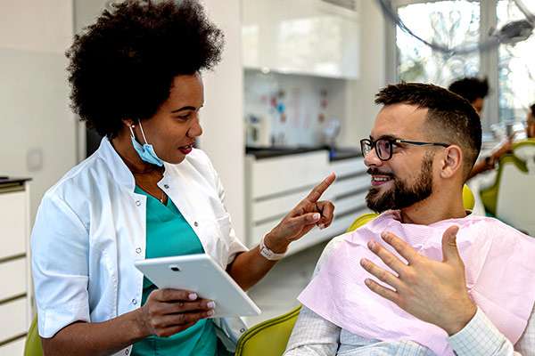 Dentist instructing a male patient with glasses, on dental insurance, while holding a digital tablet.