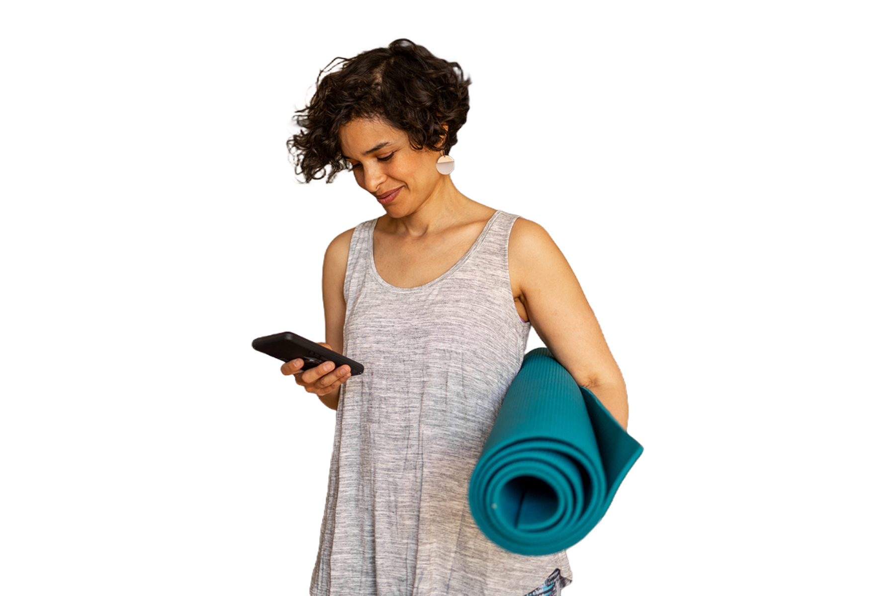 A  woman with short brown hair, in a grey tank top, looking at her phone, while holding a yoga mat.