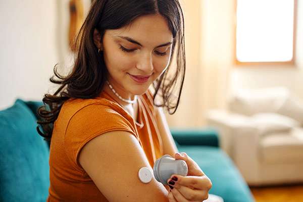 Woman in an orange top applying glucose sensor on arm at home.