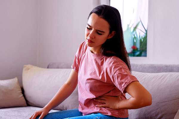 Woman sitting on a couch, clutching her side, experiencing kidney problems