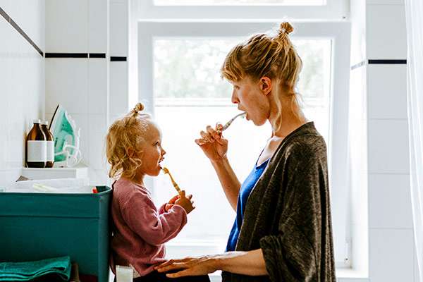 Mother teaching her toddler daughter how to brush her teeth in a clean and well lit bathroom.